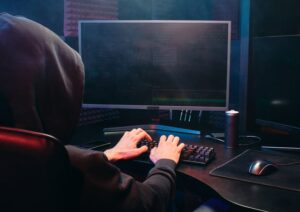 phishing hacker wearing dark hooded sweatshirt at desktop computer